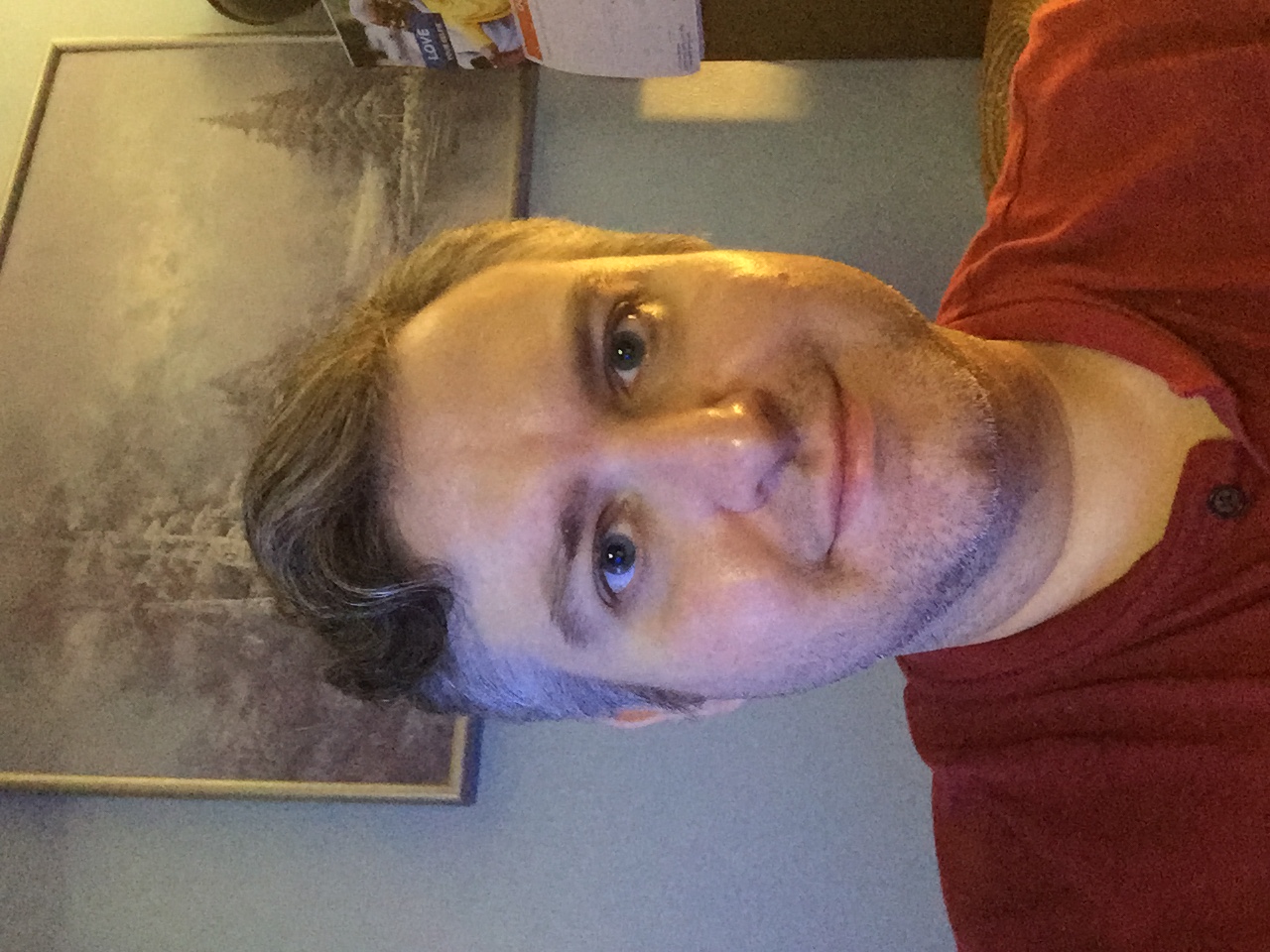 Portrait of Normand Theriault, smiling, in a red henley shirt.